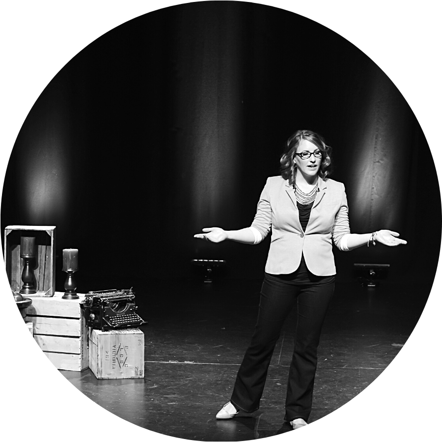 Parrish Wilson, a white skinned woman, is standing on a stage wearing black jeans and and a lighter blazer. The image is in black and white.